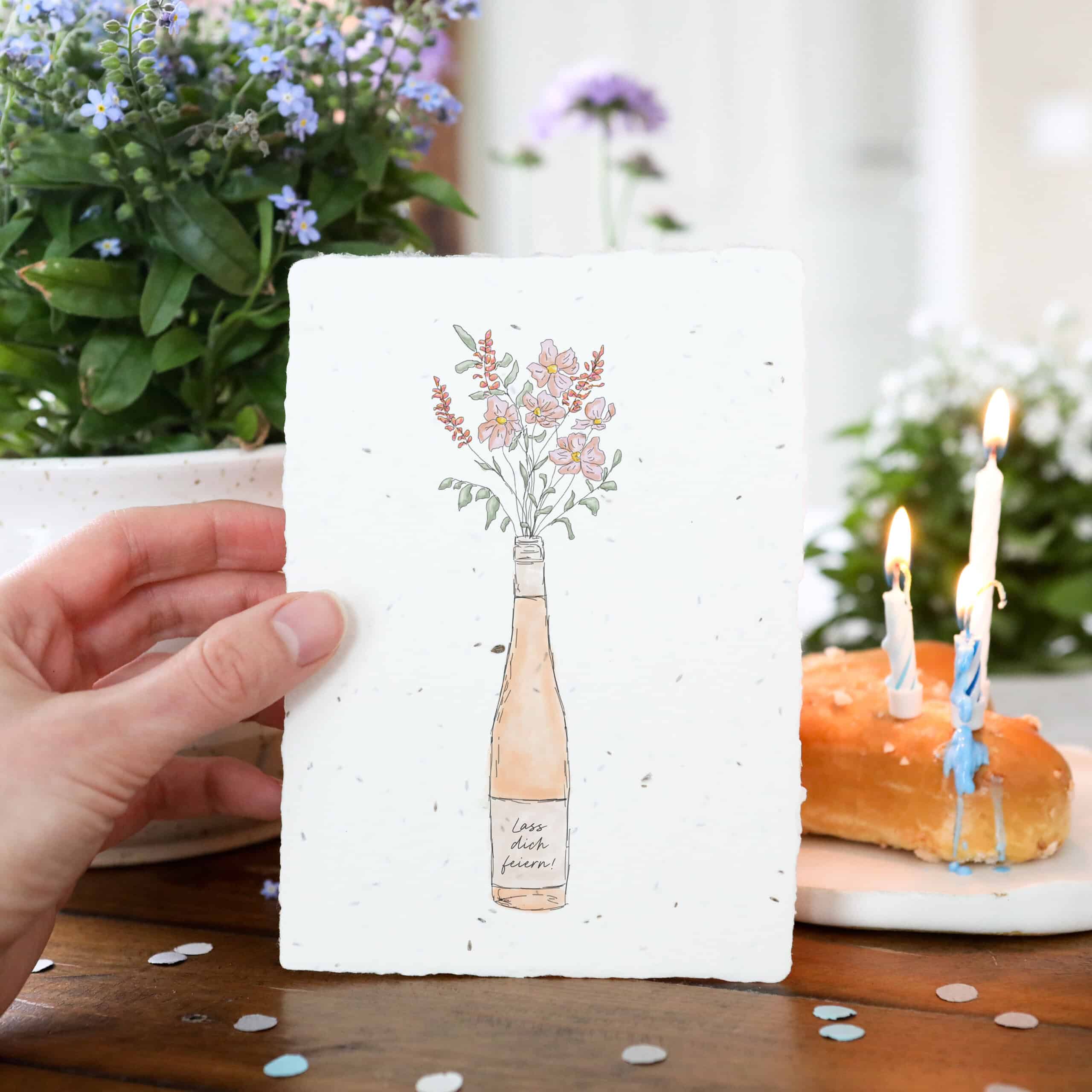 Samenkarte mit Roséwein-Flasche und Blumenstrauß sowie Aufschrift "Lass dich feiern!"