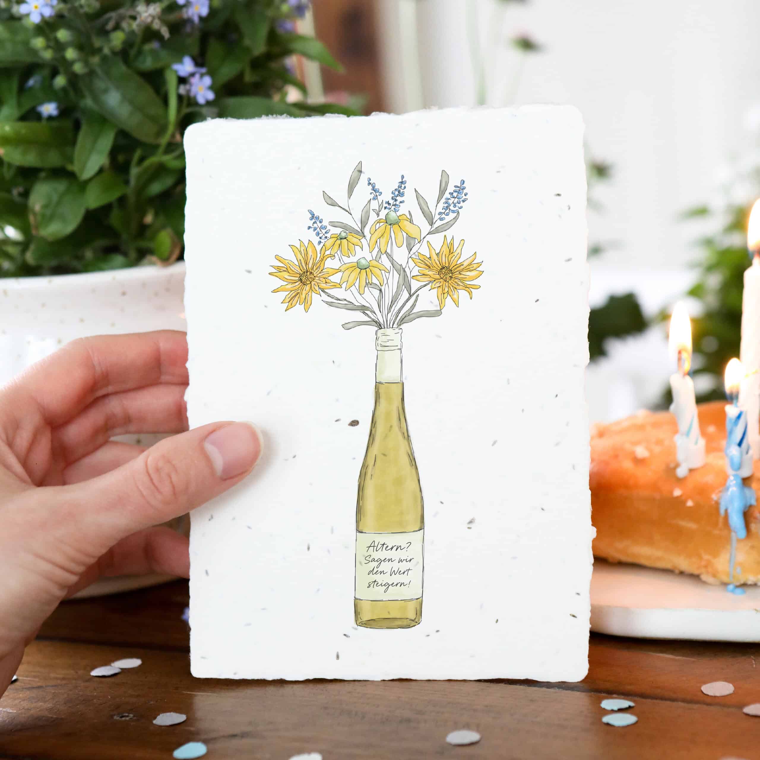 Samenkarte mit Weißwein-Flasche und Blumenstrauß sowie Aufschrift "Altern? Sagen wir den Wert steigern!"