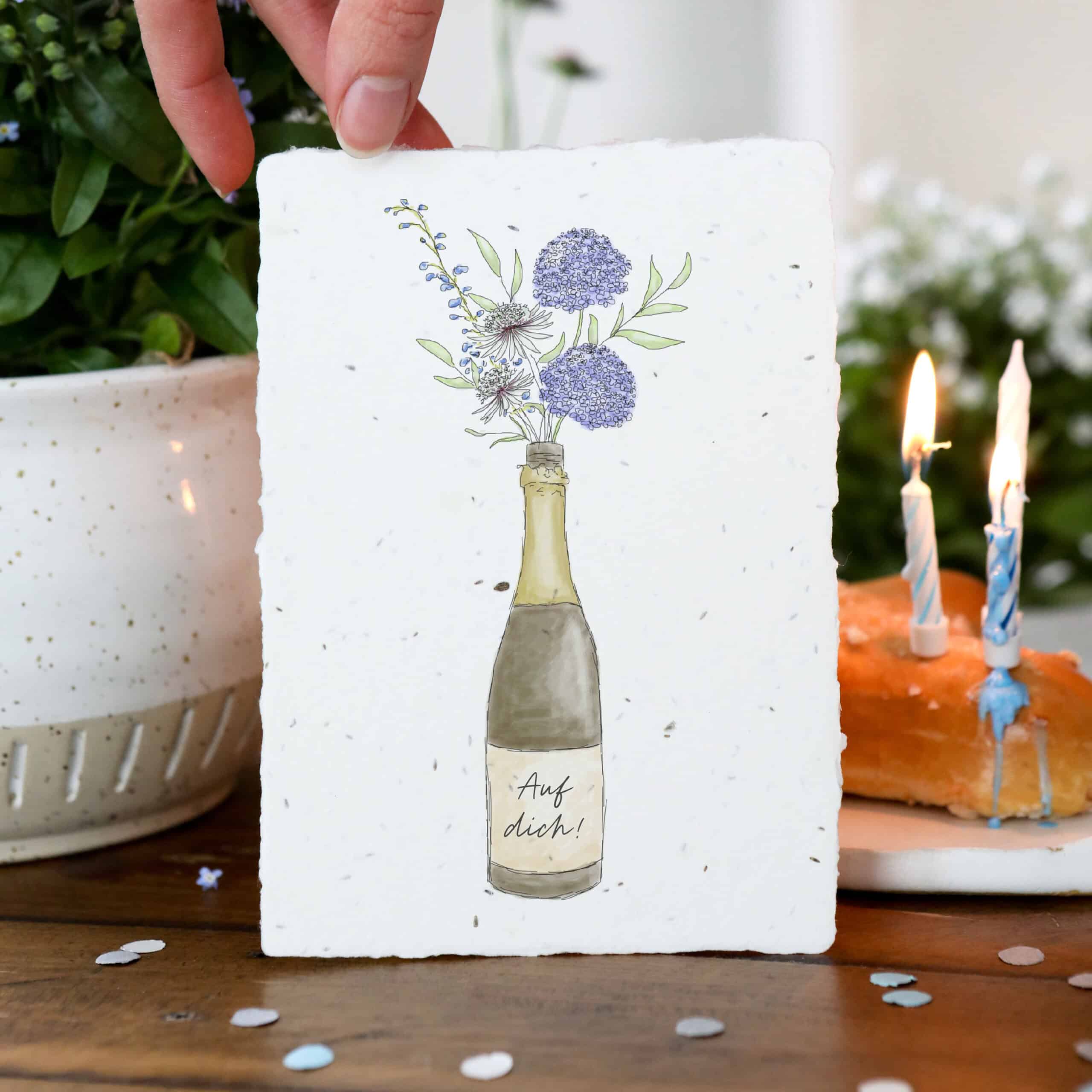 Samenkarte mit Sektflasche und Blumenstrauß sowie Aufschrift "Auf dich!"